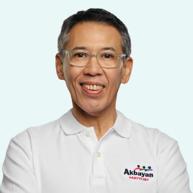 Portrait of a smiling man with glasses wearing a white shirt featuring the Akbayan Partylist logo.